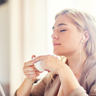 A young woman smiling and listening to music while drinking tea.