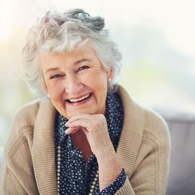An older woman smiling with her chin resting on her hand.
