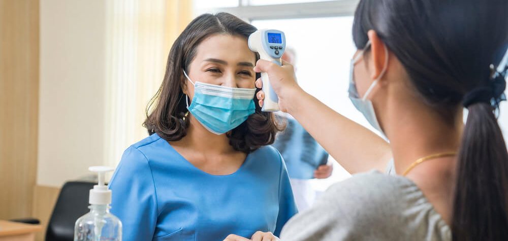 A patient getting her temperature checked while wearing a mask.