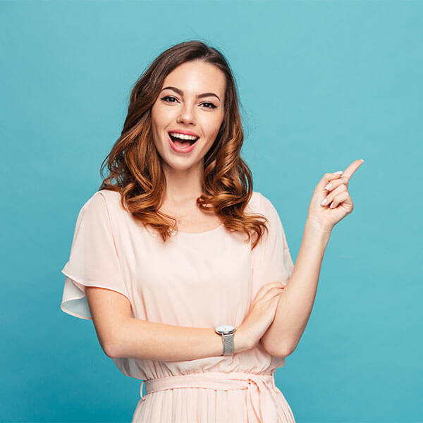 A young woman smiling and pointing her finger up in front of a blue background.